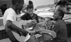 music education and youth development grants: group of young black students learning to play guitar in classroom
