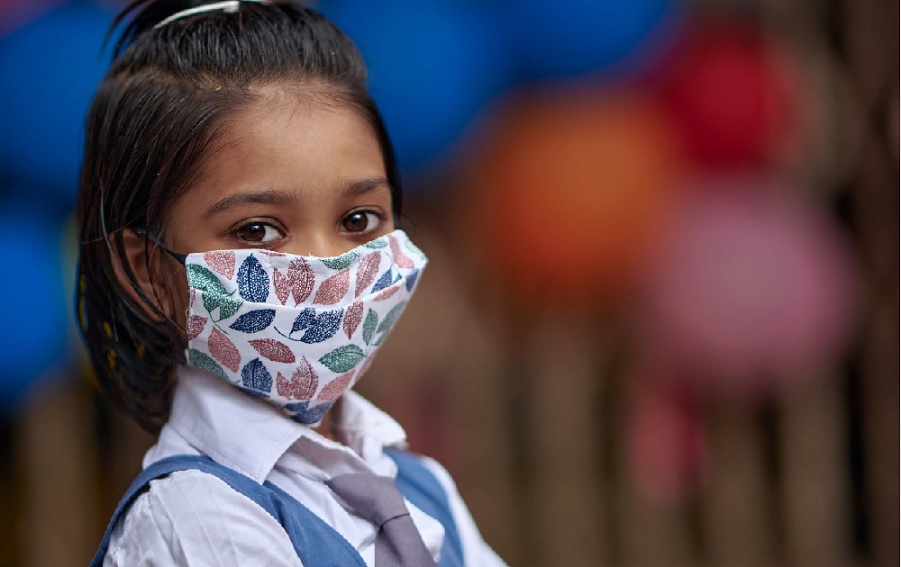 Recovering learning report: young ethnic girl looking at camera with patterned facemask on