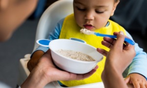 Supplemental nutrition, WIC, food access: baby with yellow bib being fed porridge