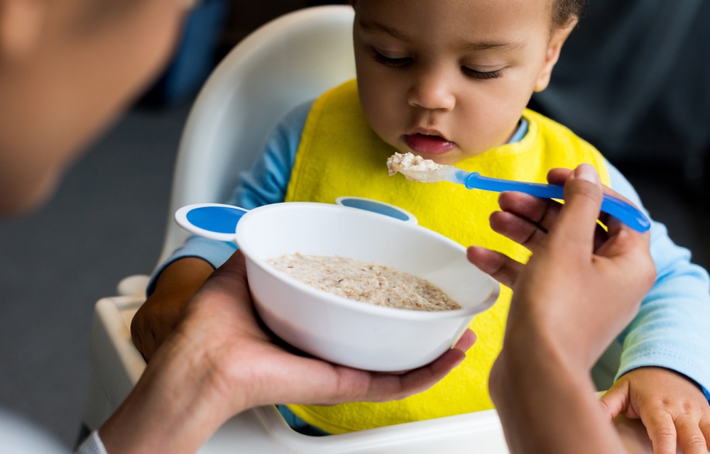 Greater Boston disadvantaged community safety net grants: baby with yellow bib being fed porridge