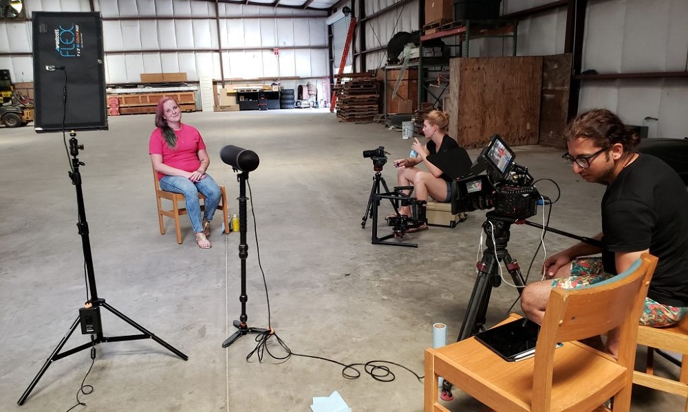 Being Michelle documentary: three people sit at filming setup with cameras and mics in a big warehouse 