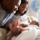 Baby Bonds plan aims to narrow wealth gap: mother and father looking down at baby