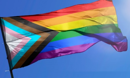 Wisconsin school board pride flag ban: progress pride flag waving in wind against blue sky