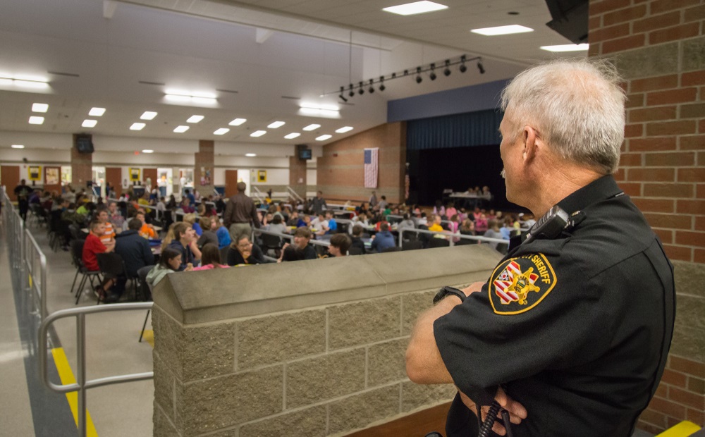school police debate: school security guard looks out over cafeteria full of students