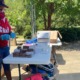 Alabama food deserts: woman in red shirt, mask and hat behind table with boxes and supplies on it