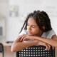 Black girls record rates of self-injury and suicide: young black girl sitting backwards in chair in classroom looking off to the side sadly
