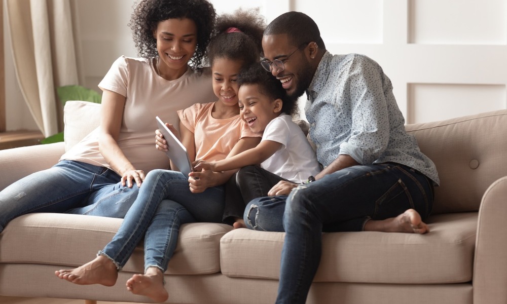 family services, economic mobility and healthy homes grants: young black family on couch laughing while looking at tablet device