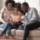family economic mobility and health grants: young black family on couch laughing while looking at tablet device