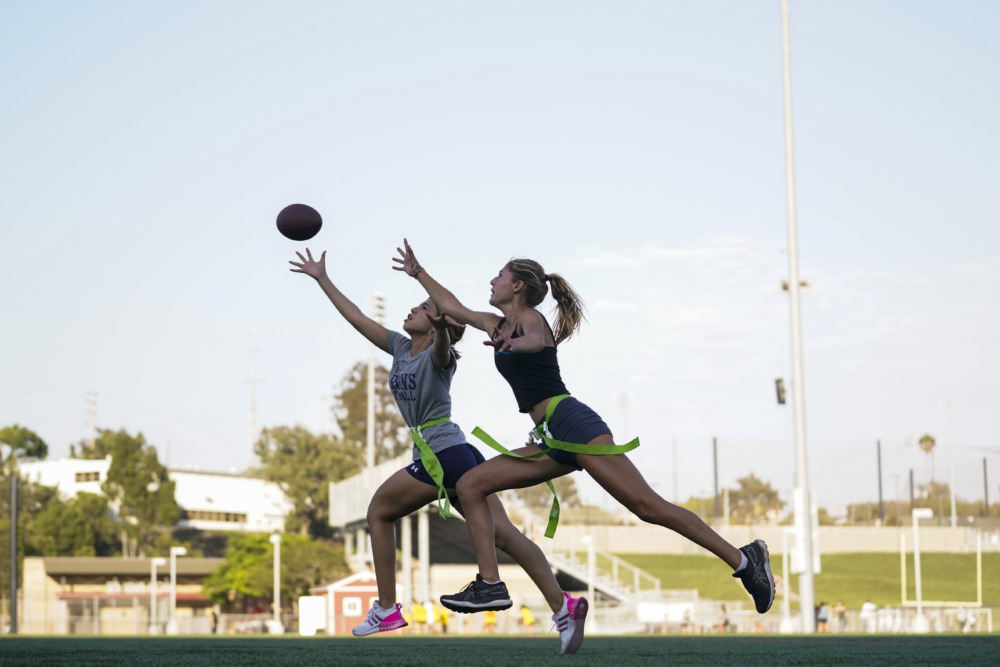 Girls' flag football: Two teen girls chasing football down playing field