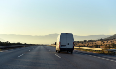 Gooning: Rear view of Silver high top cargo van traveling diwn empty highway in arid landscape toward low hills