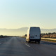 Gooning: Rear view of Silver high top cargo van traveling diwn empty highway in arid landscape toward low hills