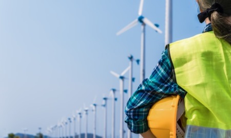 green jobs: woman engineer in reflective vest holding hard hat and looking at wind turbines