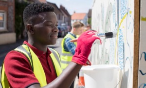 community project grants: black boy with gloves on paints an outdoor wall