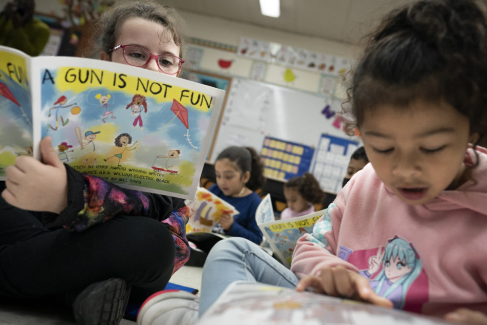 Children's Books Gun Violence: Two young childree reading large, illustrated books about gun violence