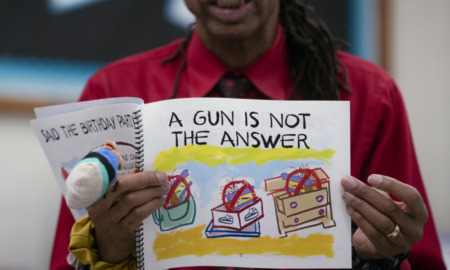 Children's Books Gun Violence: Black man in red shirt holfing a book titled, "A Gun is Not the Answer"