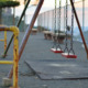 Child Abuse Reporting: Ols, rust playground swings on fenced, asphalt playground