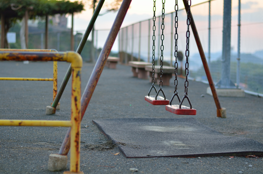Child Abuse Reporting: Ols, rust playground swings on fenced, asphalt playground