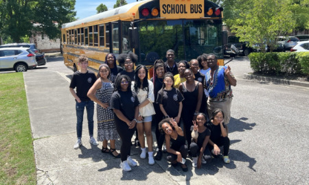 Afterschool program funding: Large group of children stand in front of yellow schoolbus with teachers in school parking lot