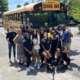 Afterschool program funding: Large group of children stand in front of yellow schoolbus with teachers in school parking lot