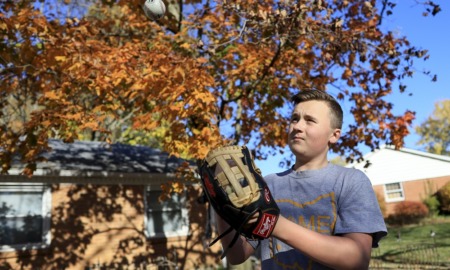 Inflation squeezes already pricey kids sports: boy with baseball glove looking at ball in the air in front of house and tree