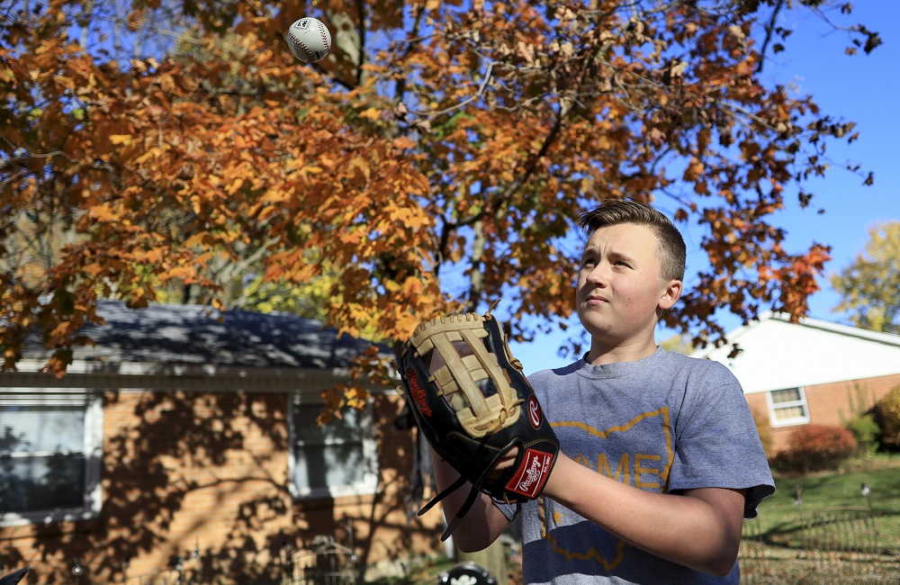 Inflation squeezes already pricey kids sports: boy with baseball glove looking at ball in the air in front of house and tree