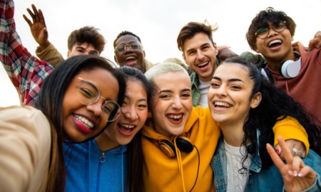 youth development: Group of nine teens stands crowded together to take a close-up selfie.