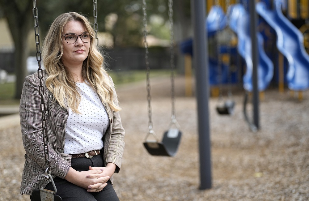 Schools struggle to staff up for youth mental health crisis: female teacher with long hair and glasses sitting on swingset swing