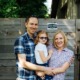 specialized dental care for disabled youth: parents smiling while holding child wit sunglasses in front of wooden fence