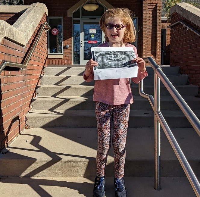 specialized dental care for disabled youth: girl with sunglasses standing on steps holding scan of her mouth