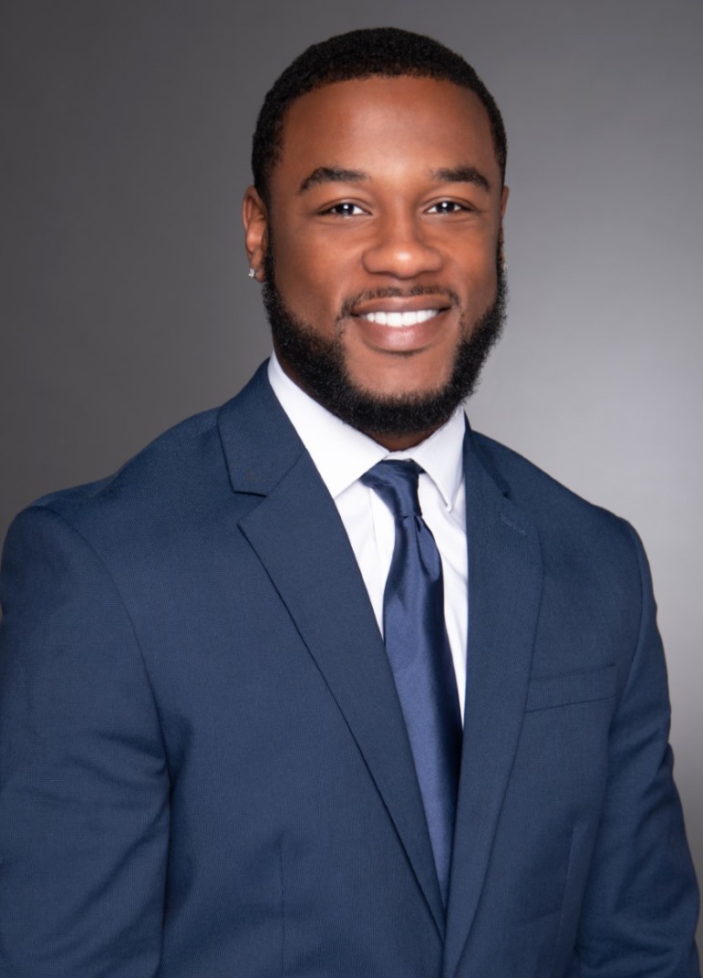 Stephon Avery Headshot: black man with black hair and beard in slate blue suit and tie with white shirt