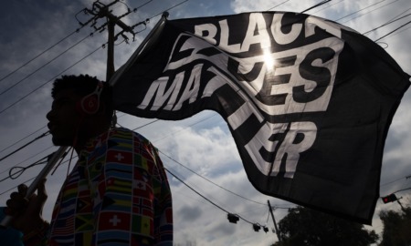 BLM sets up student relief fund as loan forgiveness stalls: man in shirt covered in flags holding a Black Lives Matter flag
