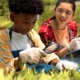 Gulf coast K-12 environmental education grants: black boy using magnifying glass to study among plants while Asian girl takes notes