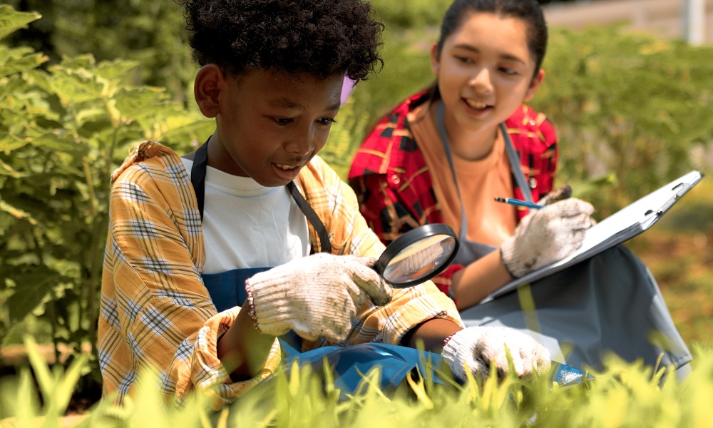 positive youth development, sparks, environmental education grants: black boy using magnifying glass to study among plants while Asian girl takes notes