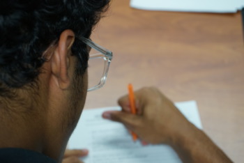 Utah College Classes: Dark-haired person with glasses and orange pencil writes on white paper