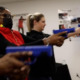 Female gun use: Two women aiming blue plastic handguns at targets during indoor training session
