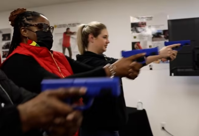 Female gun use: Two women aiming blue plastic handguns at targets during indoor training session