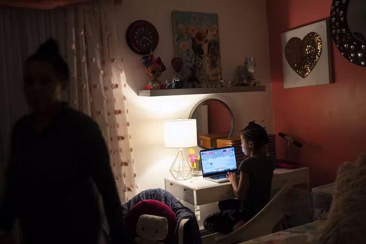 School Snoe Dats: Young girls sits at laptop on small desk in dimly lit room