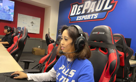 Esports: Young woman wearing headset sits at large computer screen in gaming room with multiple computers.