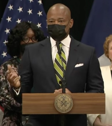 NY dyslexia program: bald black man with black facemask talks at podium with hand motioning