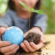 Environmental education grants: little girl holding globe and newly sprouted tree in soil