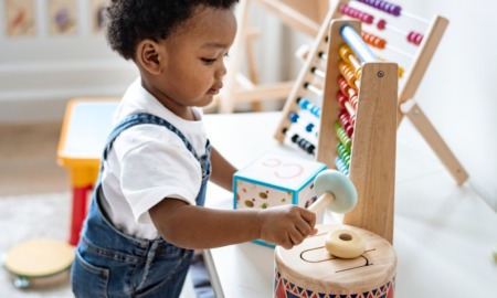 early child care and early education: young black boy in overalls playing with different colorful toys