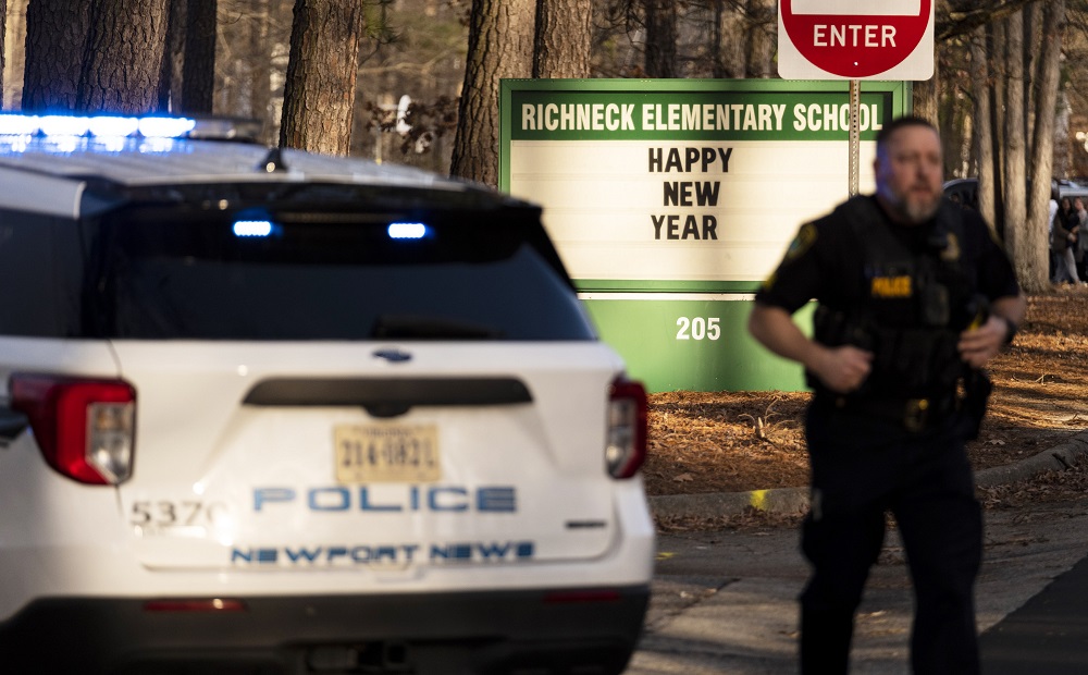 teacher shot by 6-year old 'red flag' for country: police officer stands outside school by police car with school sign in background which reads "Happy New Year"
