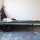 Juvenile detention populations low: Young black teen lies on bed with legs propped up on wall on cot in empty room with grey cement floor and white walls
