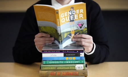 Walking on eggshells; teacher's responses to classroom limitations: person holding a book titled "Gender Queer" over a stack of other books