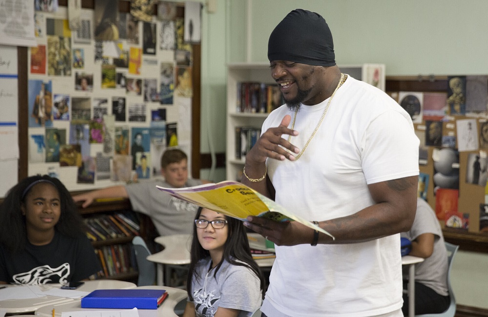 Youth program founder hurt in shooting 'has biggest heart': black man in black beanie reading happily to a classroom of students