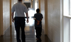 Disabled students at higher risk for arrests, dropping out: male detention worker walks a black juvenile offender down a hallway