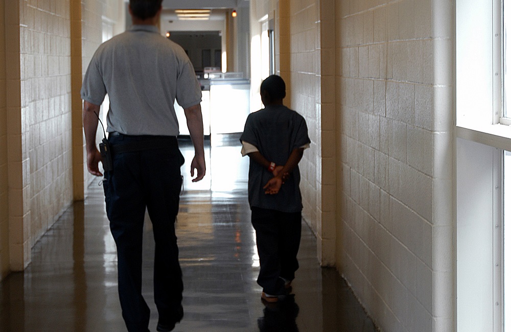 Disabled students at higher risk for arrests, dropping out: male detention worker walks a black juvenile offender down a hallway