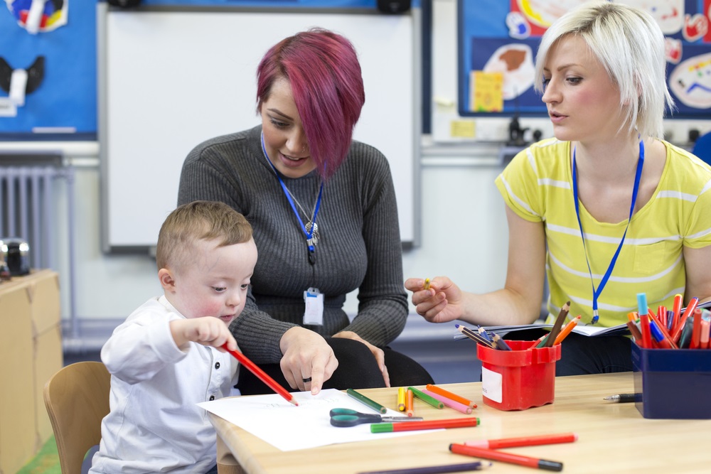 early education for children with disabilities: two teachers help a young child with down syndrome paint