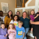 Foster care mental health: Family standing inside a house with nine children from early elementary to high school age stand closely togerher with a male and female adult.