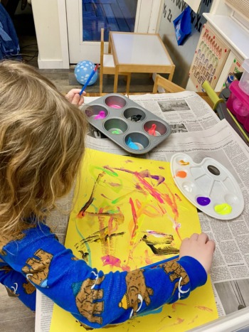 Telehealth: Young child in blue top sits at desk water coloring on yellow paper